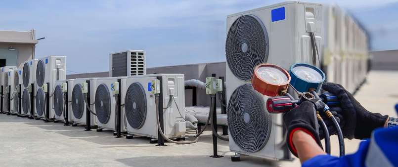 Technician servicing a rooftop bank of outdoor HVAC condenser units under a maintenance contract